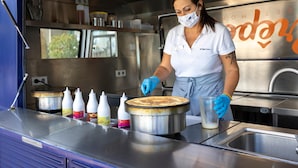 A person in a white shirt and blue gloves preparing food in a commercial kitchen with stainless steel surfaces and various condiment bottles.