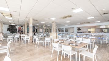 A spacious dining area with white chairs and tables, a stone pillar, and a kitchen area in the background.