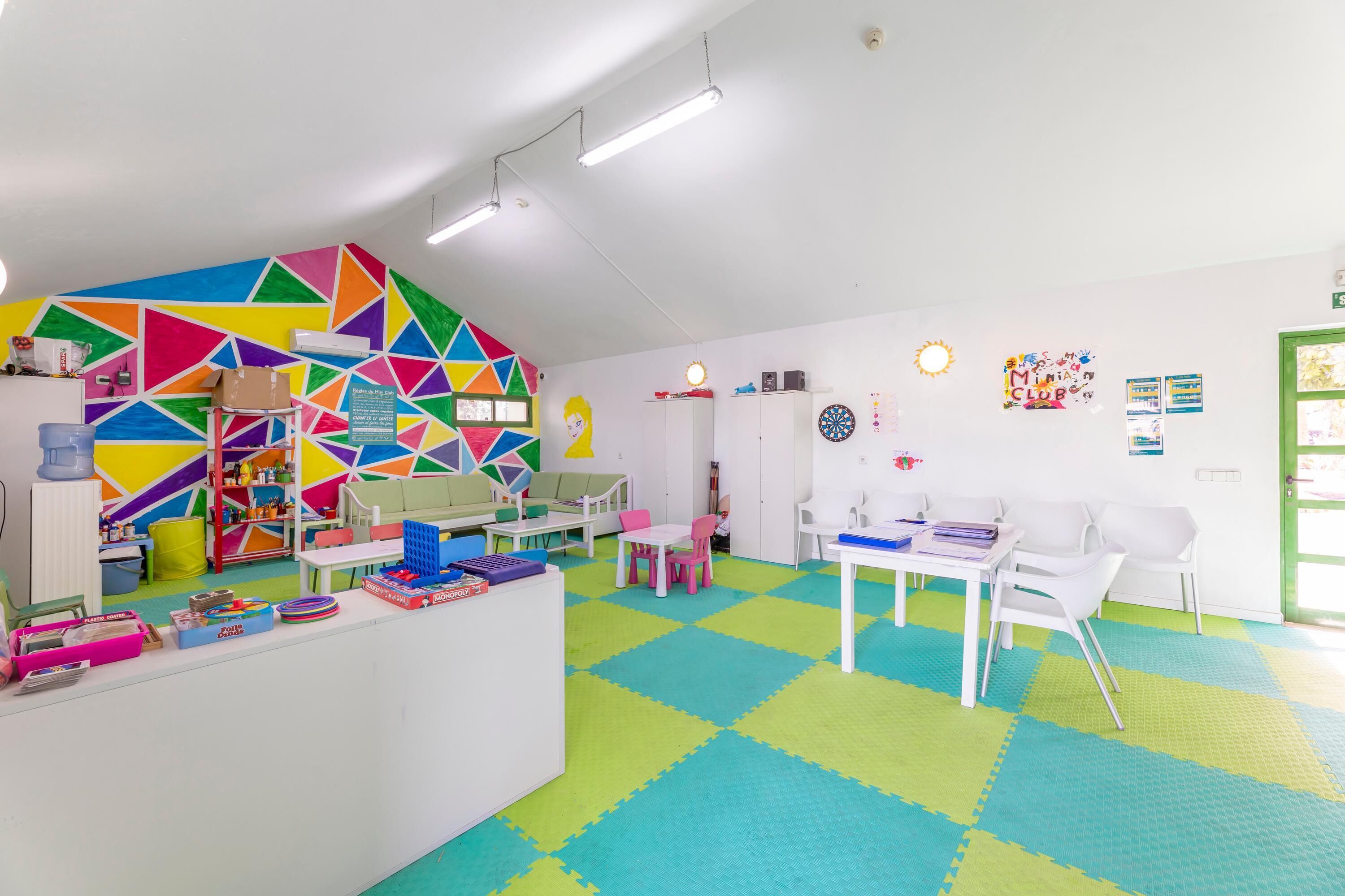 Ein helles Spielzimmer mit geometrischer Wandgestaltung, einem weißen Empfangsschalter und einer Rezeption.