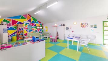 A brightly colored playroom with geometric wall art, a white reception desk, and a check-in counter.