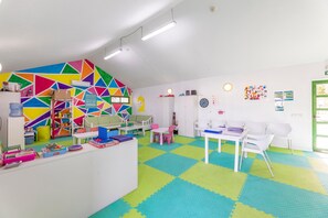 Ein helles Spielzimmer mit geometrischer Wandgestaltung, einem weißen Empfangsschalter und einer Rezeption.