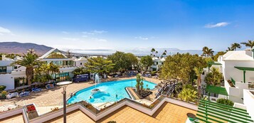 Un resort con piscina, palmeras y montañas al fondo.