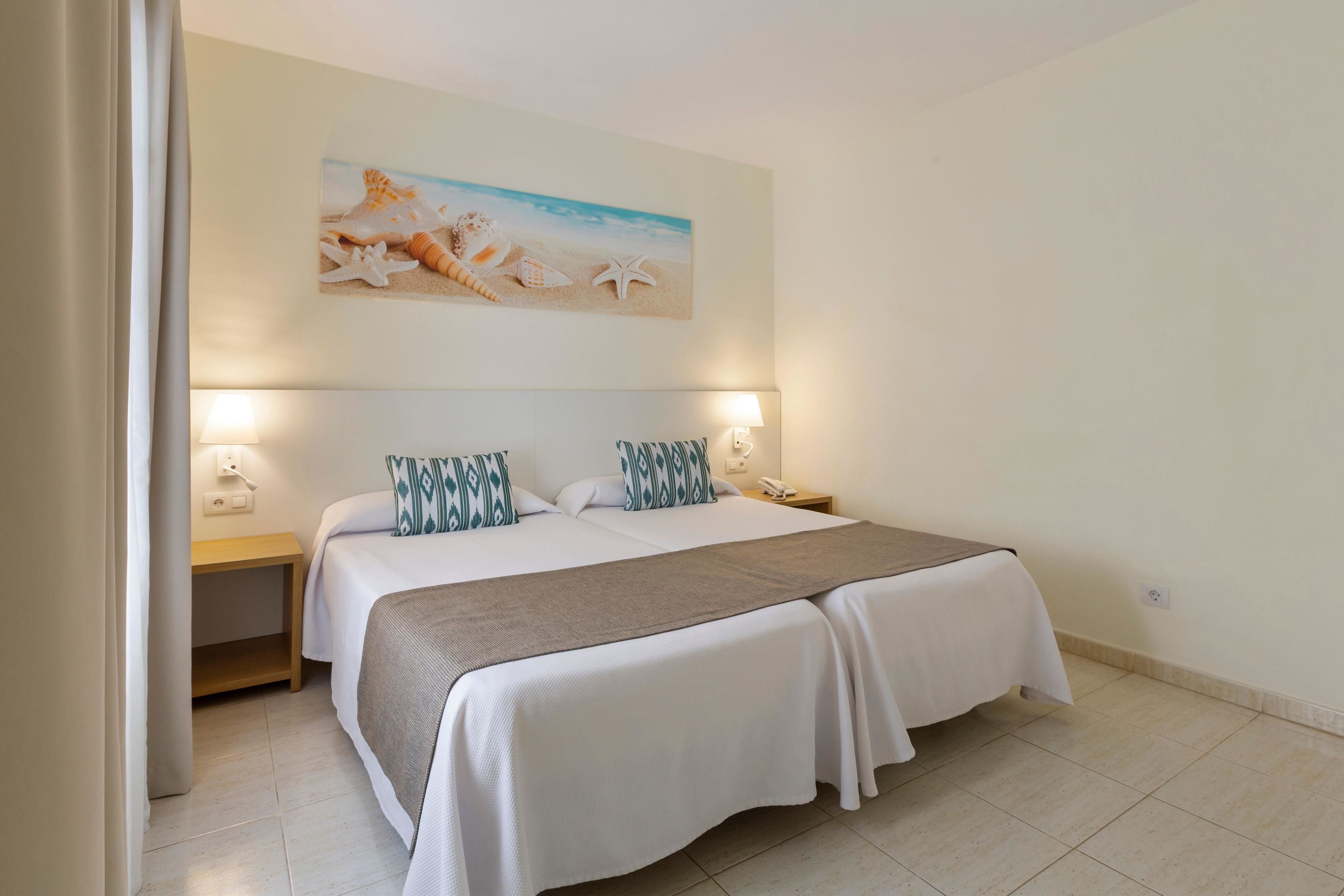 A neatly arranged bedroom with a large bed, two bedside tables, and a wall-mounted painting of a beach scene.