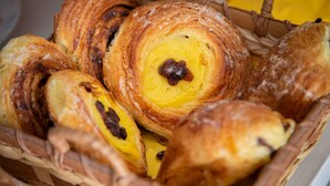 Una cesta llena de varios pasteles, incluyendo croissants y un pastel relleno de chocolate.