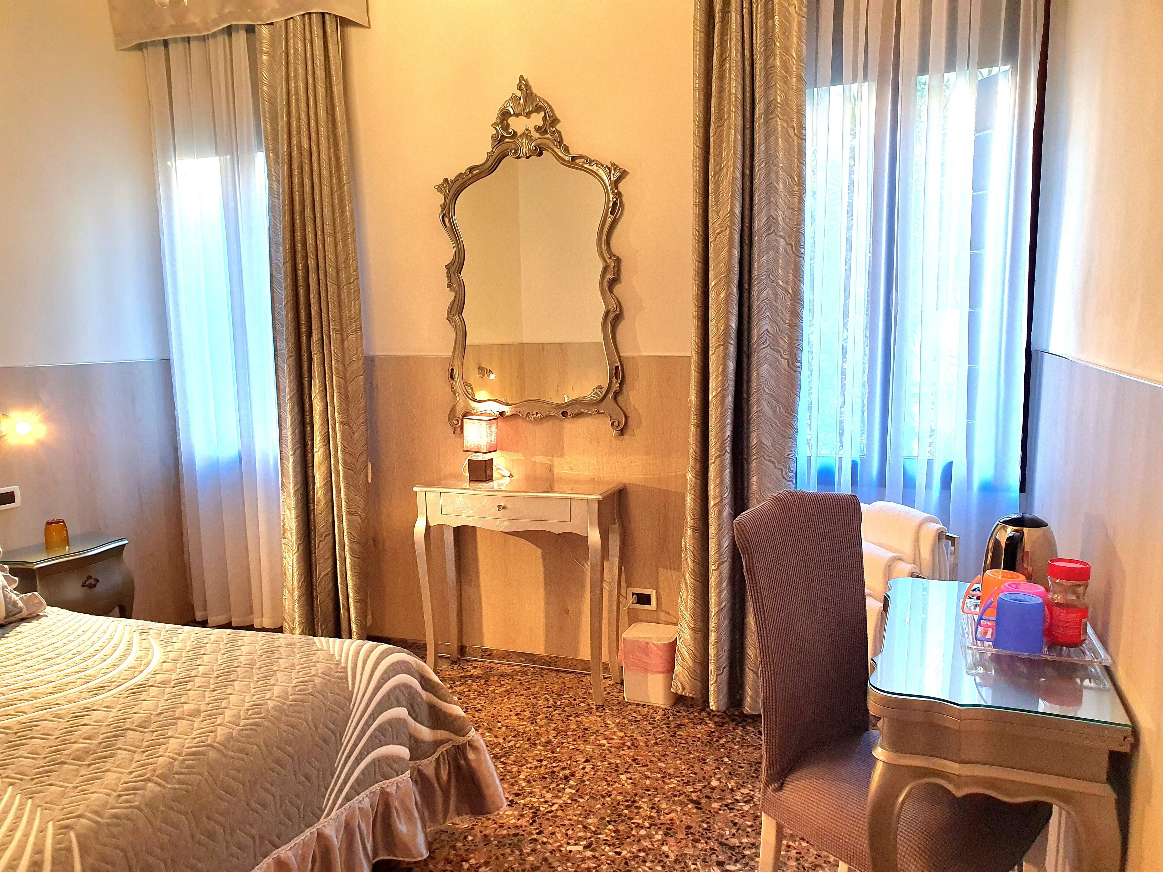 A hotel room with a bed, a desk with a lamp, a chair, and a large mirror on the wall.