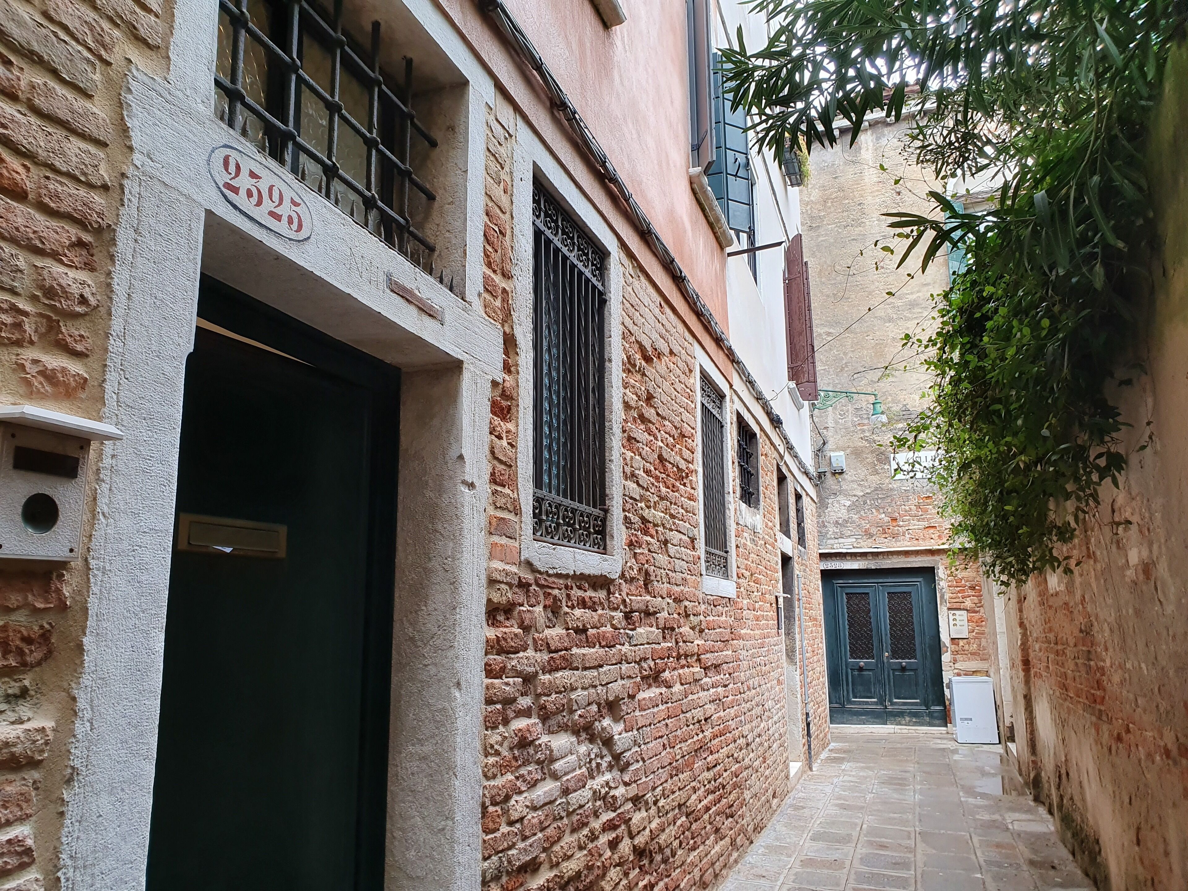 A narrow alleyway with a brick building, a black door, and a window with metal bars.