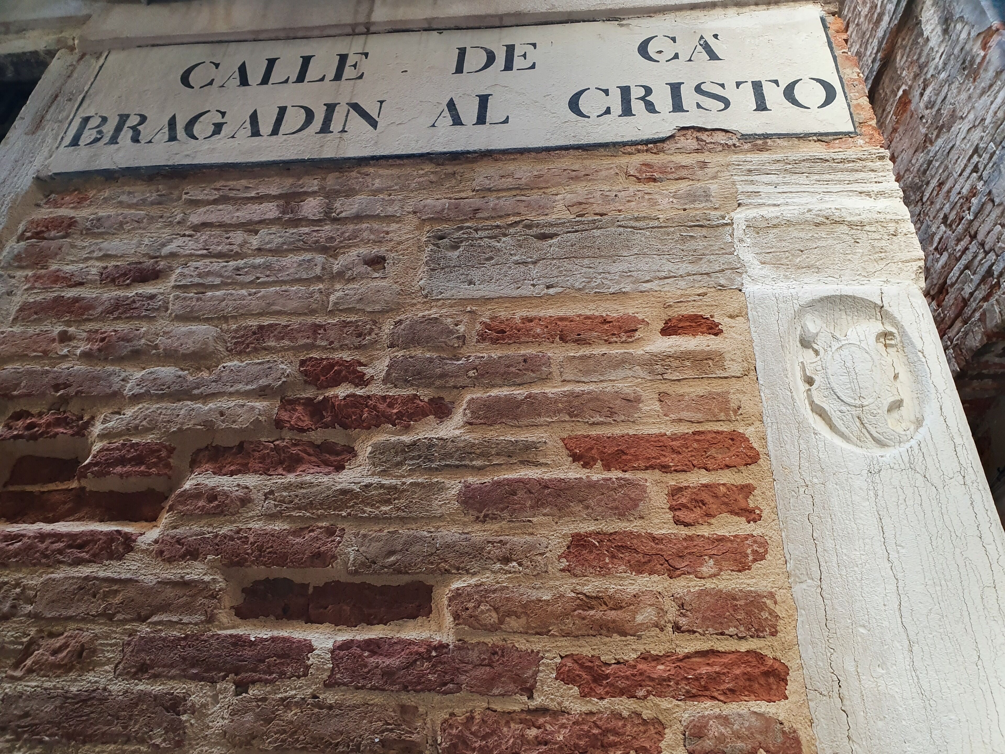 A stone wall with a plaque reading "Calle de la Bragadina al Cristo".