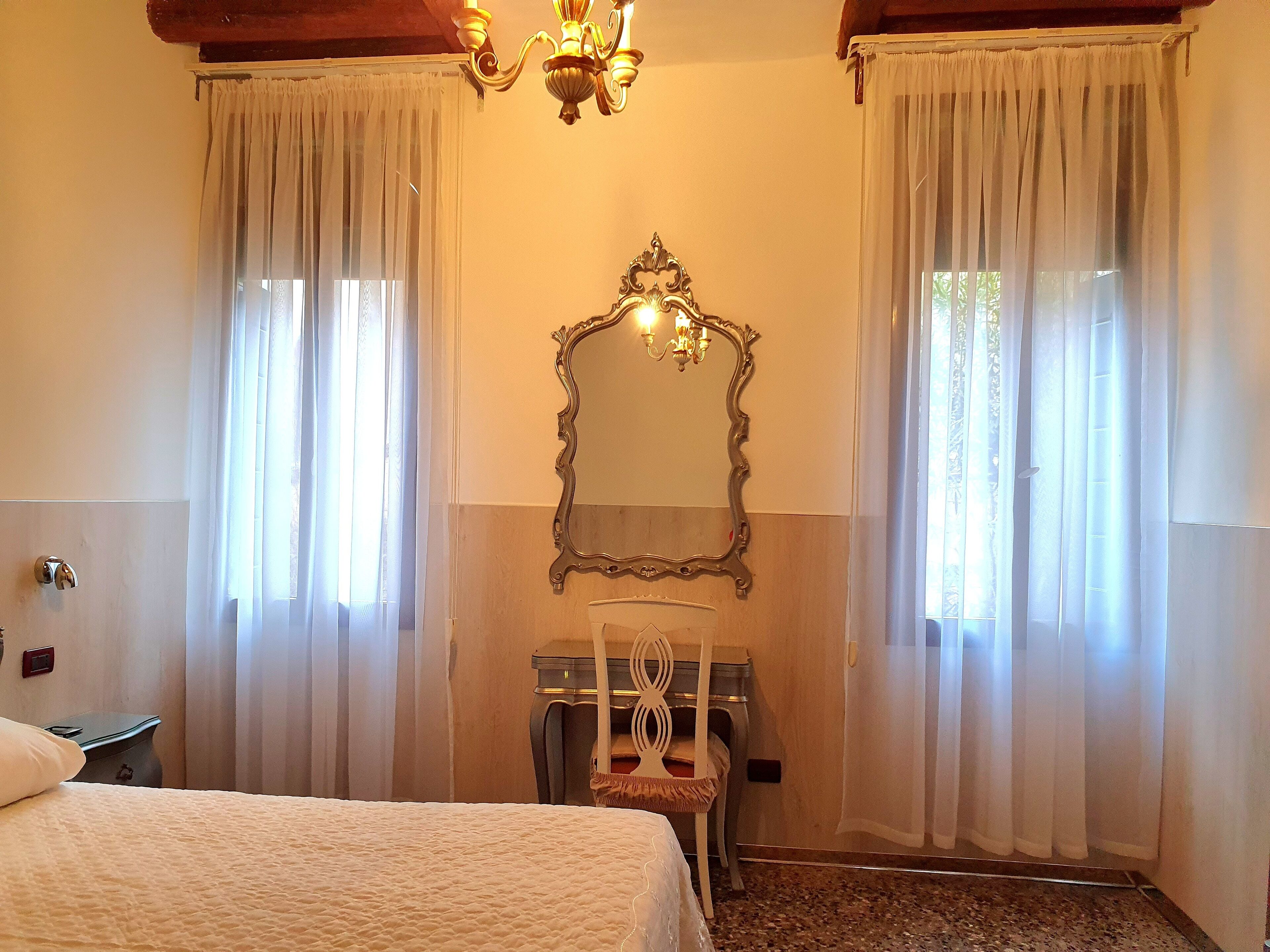 A hotel room with a bed, a vanity with a mirror, and a chandelier.
