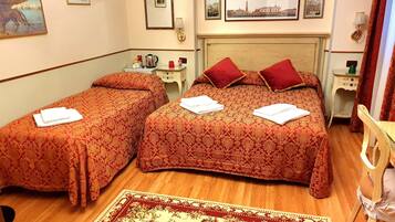 Une chambre d’hôtel avec deux lits simples, un plancher en bois, un grand tapis à motifs et un mur orné de tableaux encadrés.