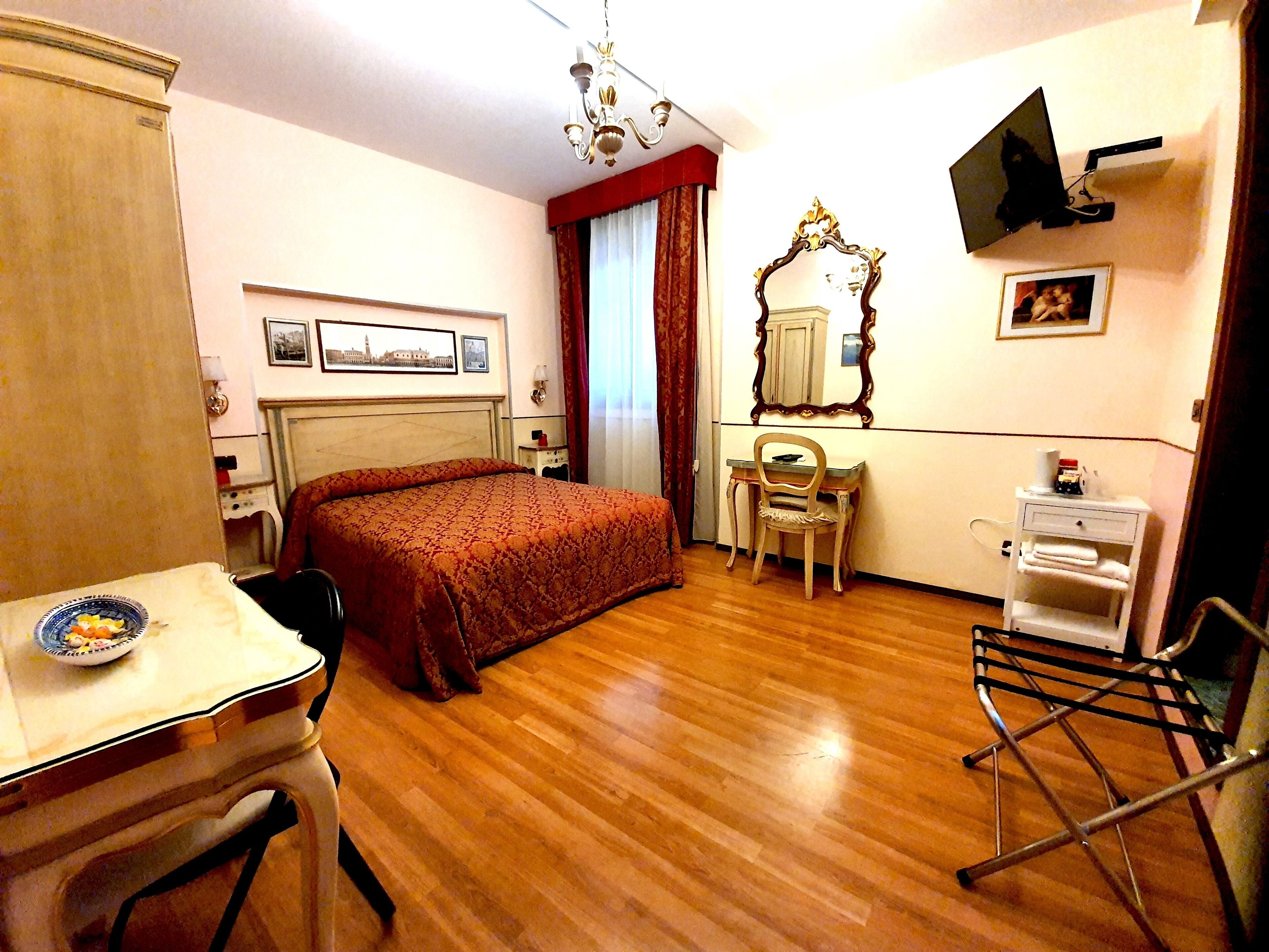 Une chambre d’hôtel comprenant un lit, un bureau, une chaise, une télévision, un miroir et une petite table avec une assiette.