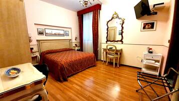 Une chambre d’hôtel comprenant un lit, un bureau, une chaise, une télévision, un miroir et une petite table avec une assiette.