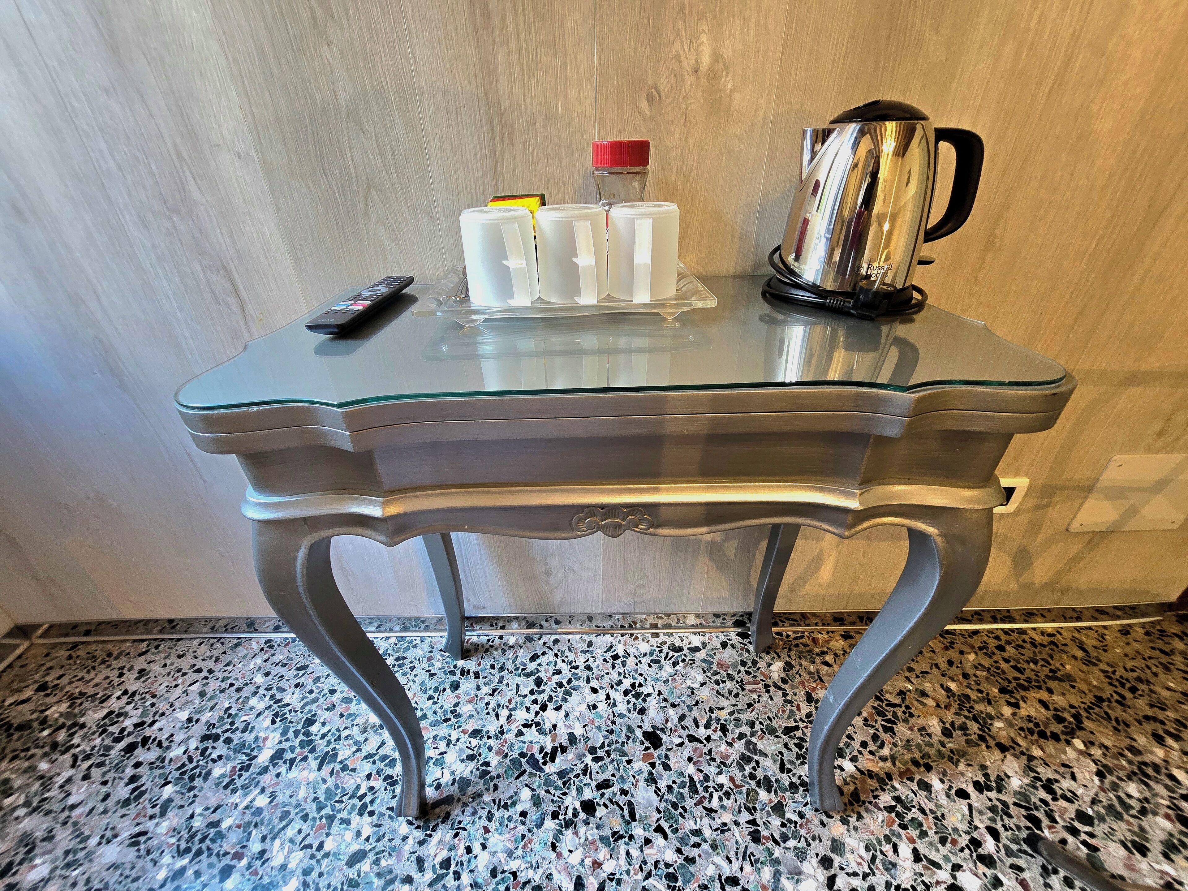 Een glazen tafel met een roestvrijstalen waterkoker, een afstandsbediening en drie witte bakken met rode deksels.