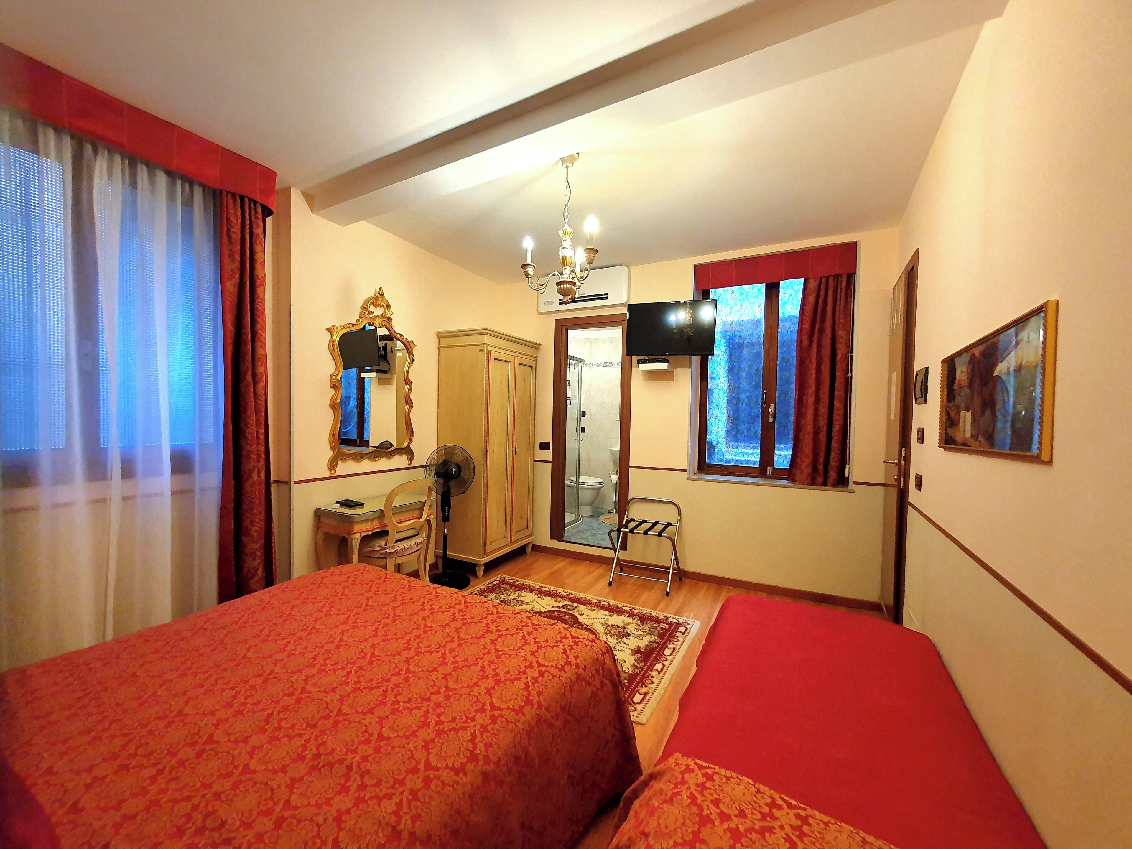 A hotel room with two beds, a desk, a chair, a TV, a mirror, and a shower area.