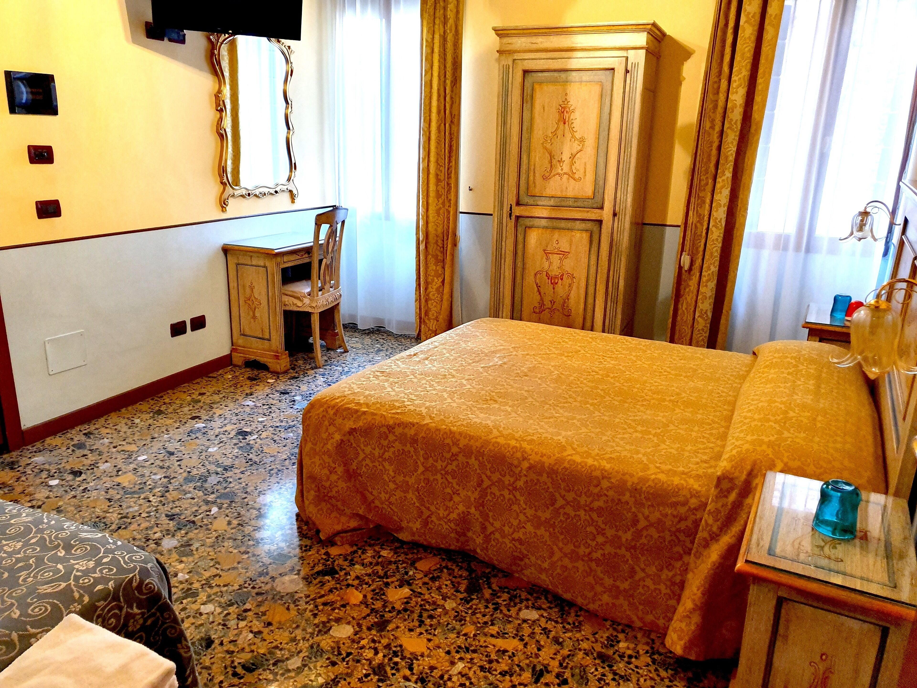 Una habitación de hotel con cama, escritorio, silla, armario y televisor.