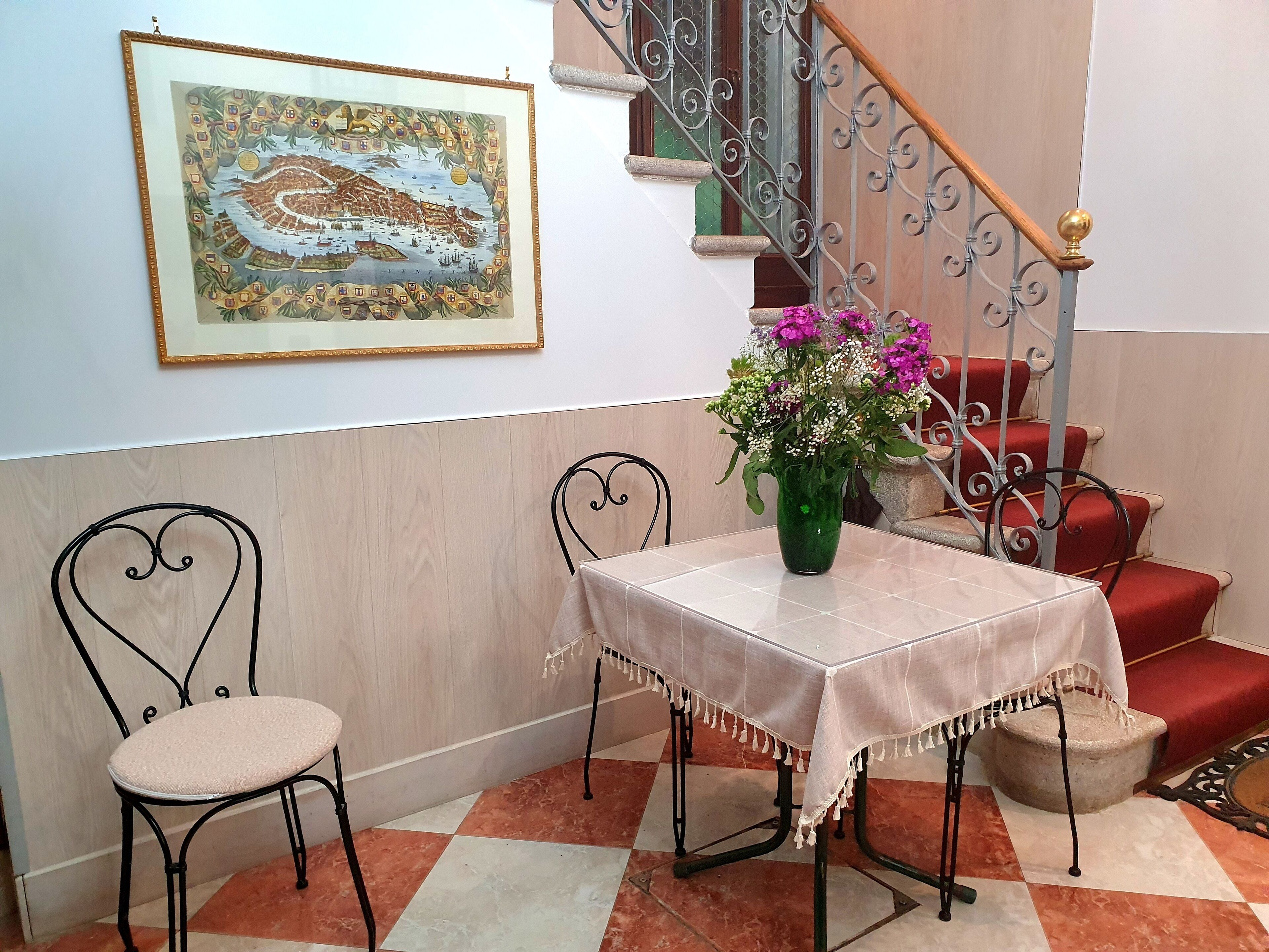 Un comedor con una mesa, sillas, un jarrón con flores, una escalera y una obra de arte enmarcada en la pared.