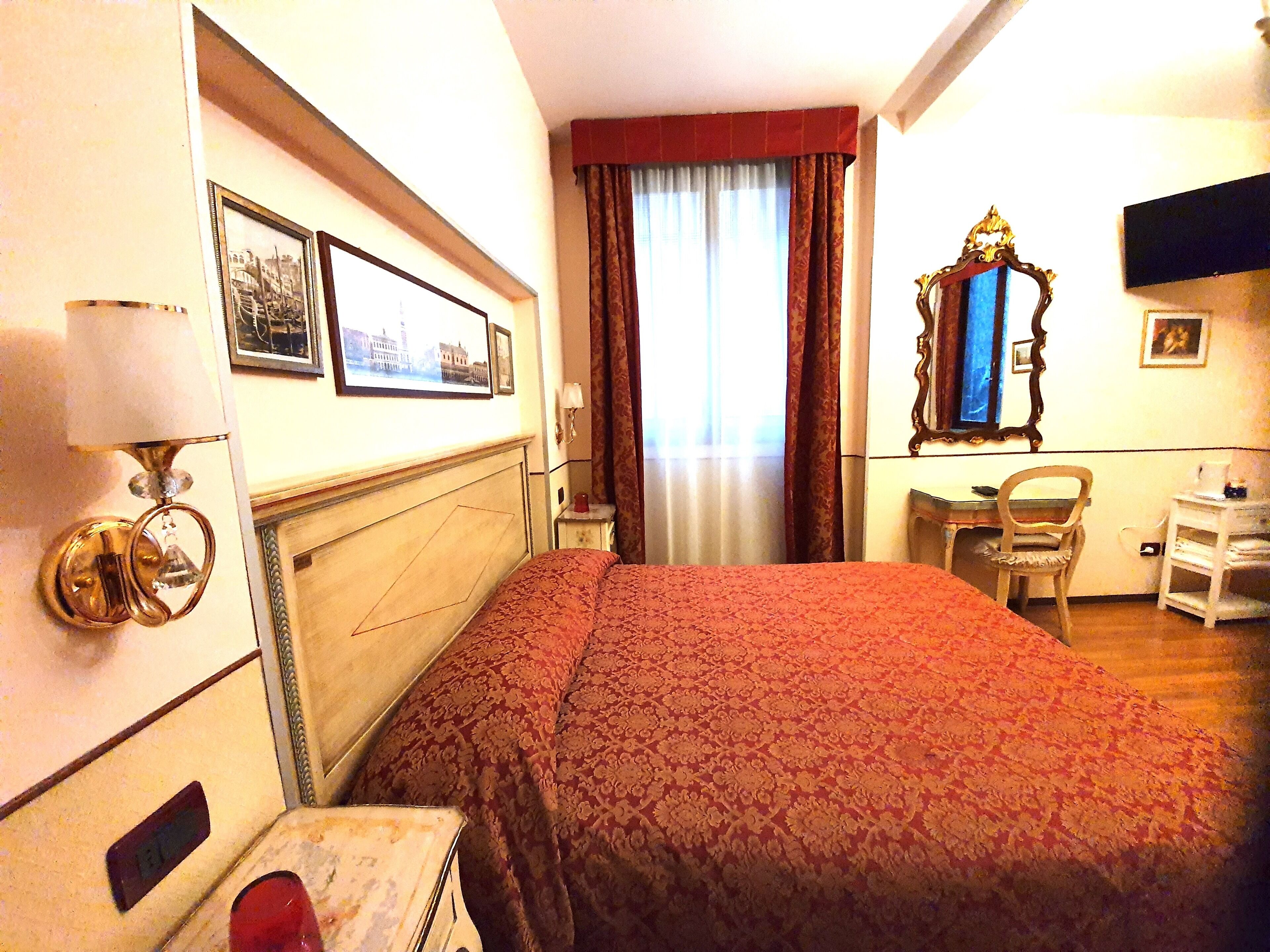 Una habitación de hotel con una cama, un escritorio, una silla, un espejo y una ventana con cortinas.
