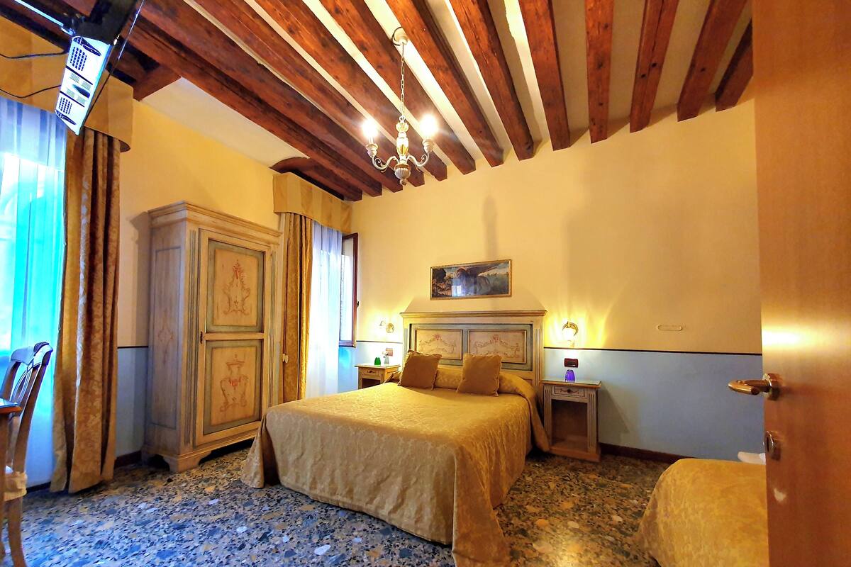 Quarto de hotel com uma cama, uma mesinha de cabeceira, uma luminária, um quadro na parede e teto de madeira.