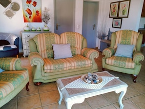 Uma sala de estar com sofás estampados, uma mesa de centro com pinhas decorativas e um quadro de flores na parede.