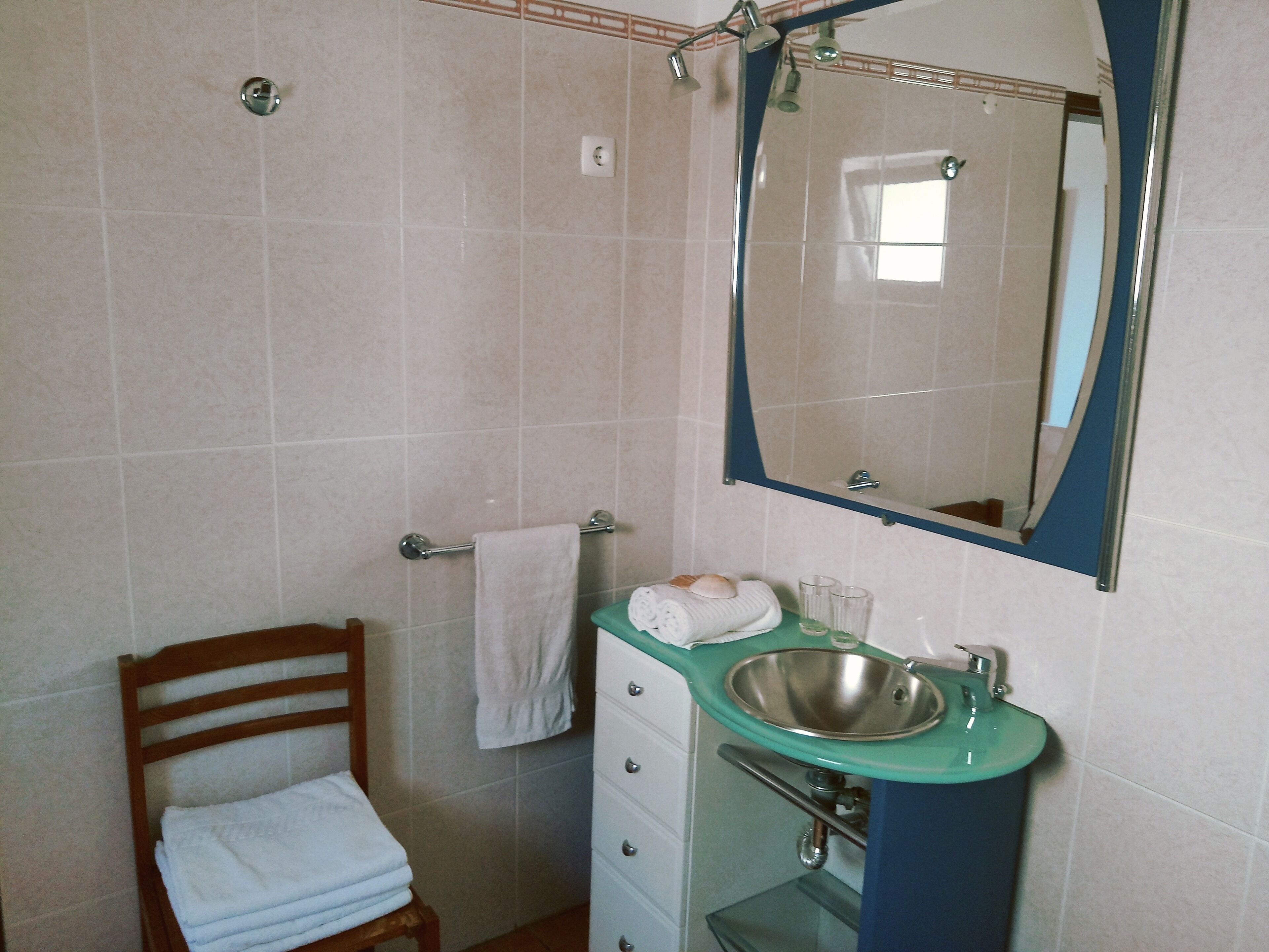 Een badkamer met een houten stoel, een wastafel en een spiegel.