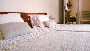 Una cama bien hecha con sábanas blancas y un patrón acolchado, un cabecero de madera y una mesita de noche con una lámpara.