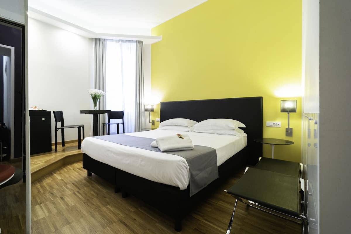 A hotel room with a bed, bedside tables, a desk, and a chair.