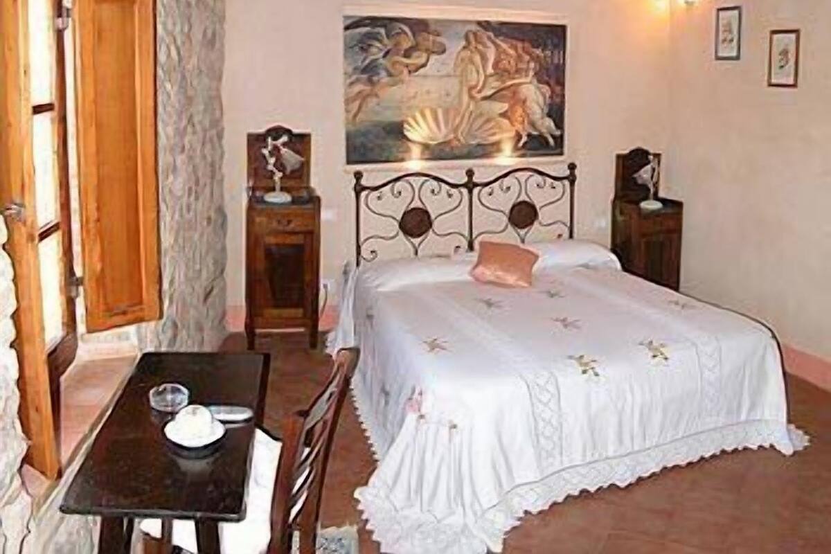 A bedroom with a bed, a table, and a painting on the wall.