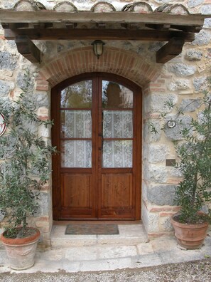 A stone building with a wooden door, two potted plants, and a small overhang above the door. - Antica Dimora (San Gimignano)