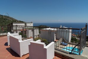 A rooftop terrace with white wicker furniture, a swimming pool, and a view of the sea.