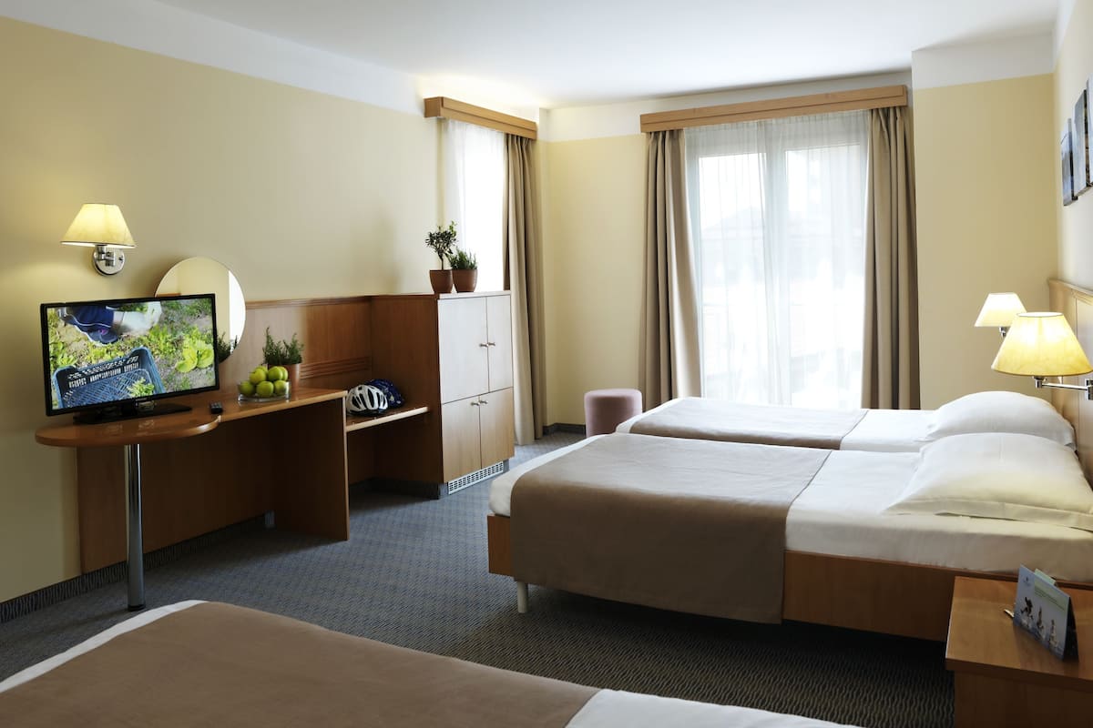 A hotel room with two beds, a desk with a TV, a small table, and a cabinet.