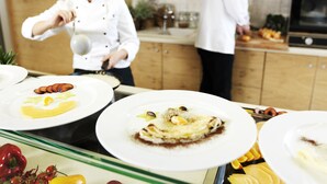 A chef preparing food in a kitchen with wooden cabinets and a tiled backsplash. - Hotel Neptun – Lifeclass Hotels & Spa, Portorož (Piran)