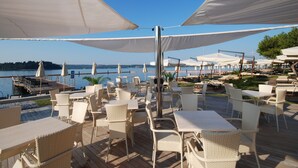 An outdoor seating area with white wicker furniture and large white umbrellas, overlooking a body of water. - Hotel Neptun – Lifeclass Hotels & Spa, Portorož (Piran)