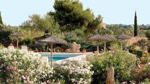 Une piscine entourée d’une végétation luxuriante et ombragée par des parasols en chaume.