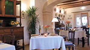 Un espace repas agrémenté de meubles de rangement en bois, d’une grande plante en pot et de plusieurs tables dressées pour le repas.