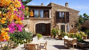 Une maison en pierre à deux étages, dotée d’un patio aménagé avec du mobilier d’extérieur.