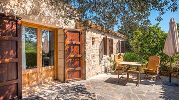 Un patio exterior con suelo de piedra, muebles de madera y pared de piedra.