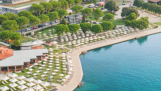 Ein Luftbild eines Küstenhotels mit Strandlounge, Pool und Steg.