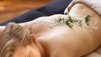 A person lying on a massage table with a towel and some herbs on their back.