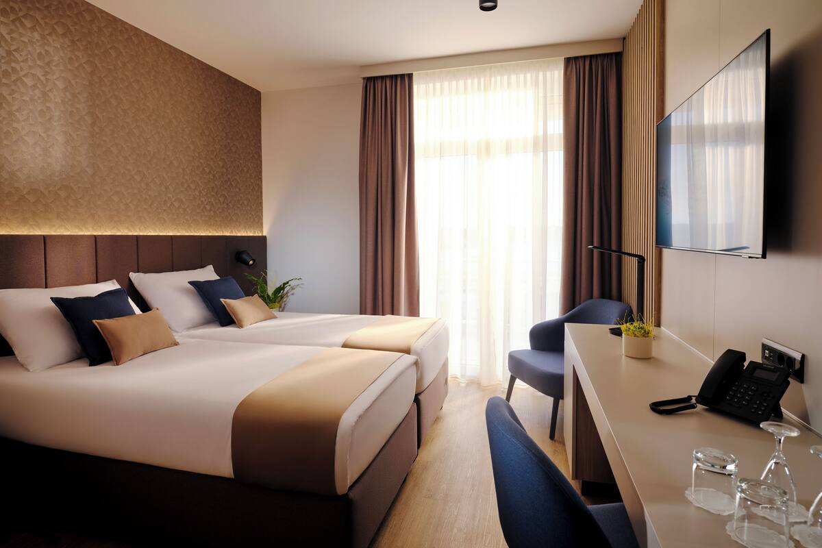 A hotel room with a large bed, a desk with a phone and glasses, and a TV on the wall.
