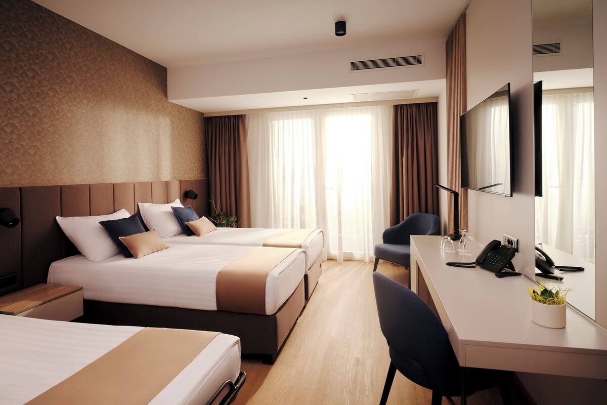A hotel room with two beds, a desk, a chair, a TV, and a phone.