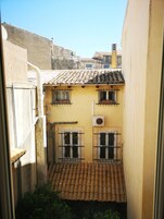 Uma viela estreita com um edifício amarelo, duas janelas com persianas de grade e um telhado telhado.