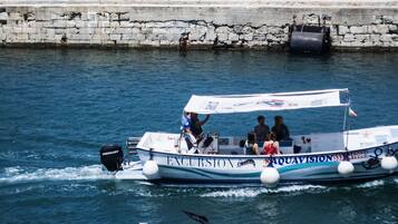 A boat named 'AQUAVISION' with passengers, moving on water near a stone wall.