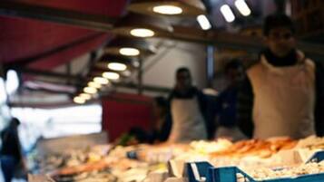 Puesto de mercado con diversos productos del mar expuestos bajo una toldo rojo.