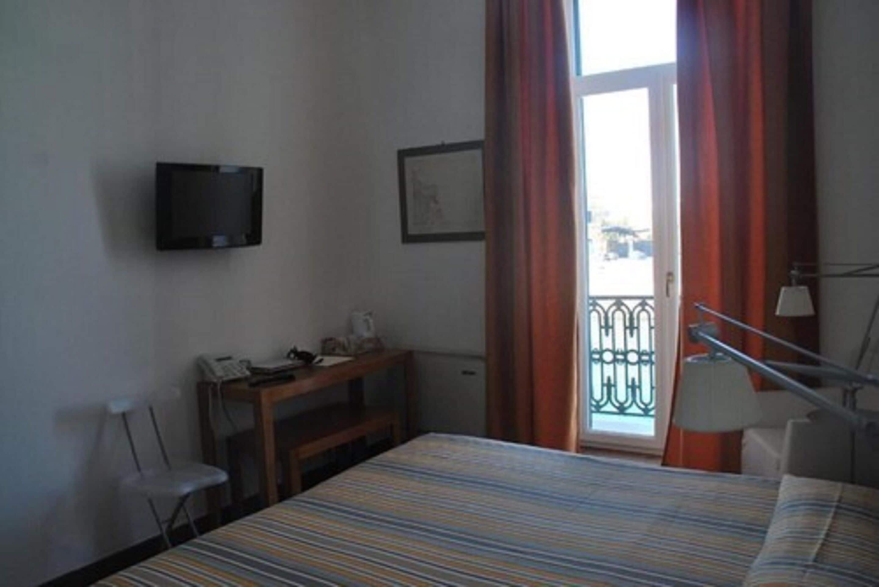 Une chambre d’hôtel comprenant un lit, un bureau avec un téléphone, un téléviseur fixé au mur et une fenêtre avec des rideaux.