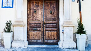 A large wooden double door with a metal arch above it, flanked by two white planters with small trees. - L'Approdo delle Sirene (Syracuse)