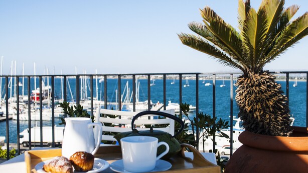 A terrace with a view of the sea, a white chair, a table with a tray of pastries and a cup, and a potted plant. - L'Approdo delle Sirene (Syracuse)