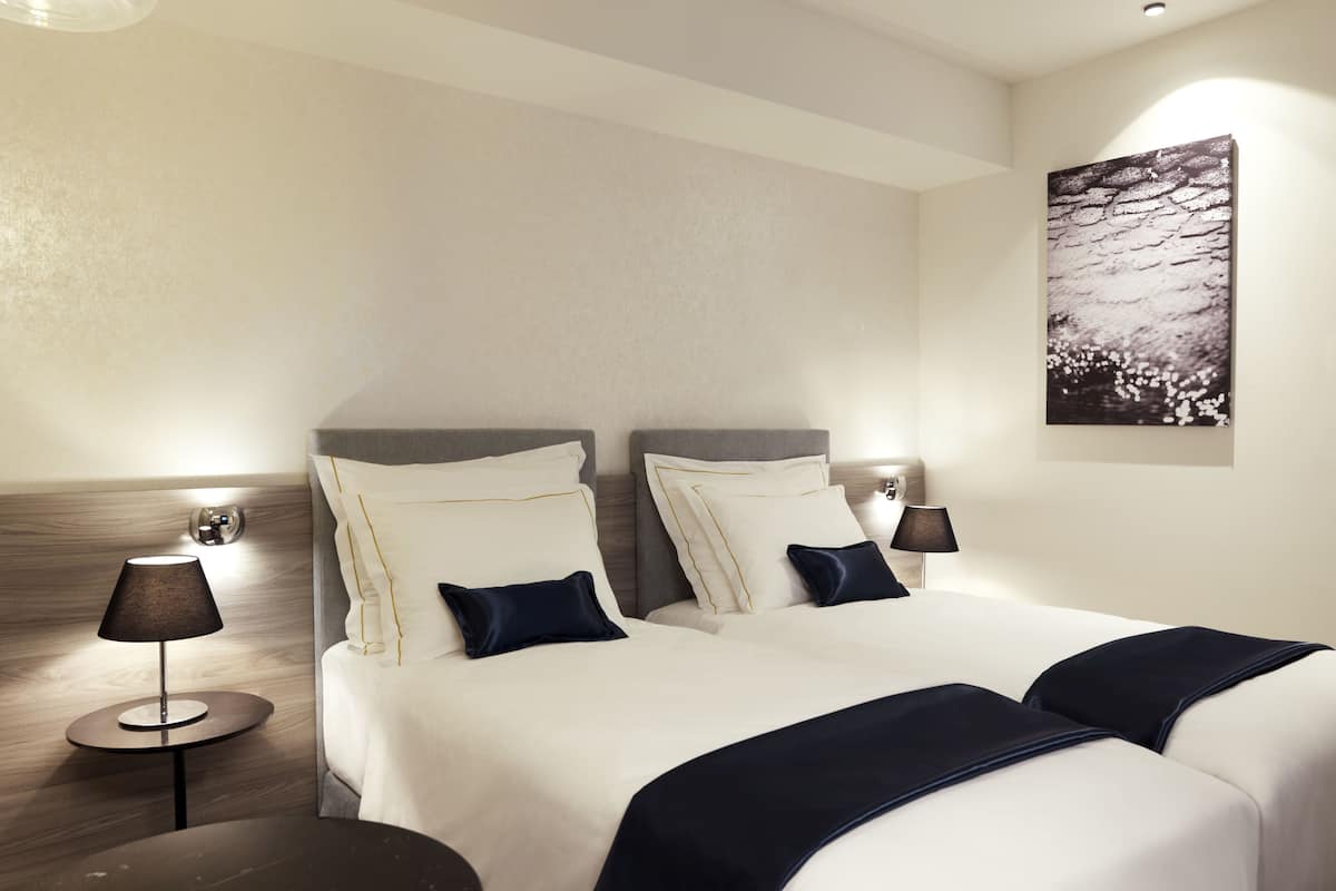 Habitación de hotel con dos camas, una mesita de noche, una lámpara y una obra de arte colgada en la pared.