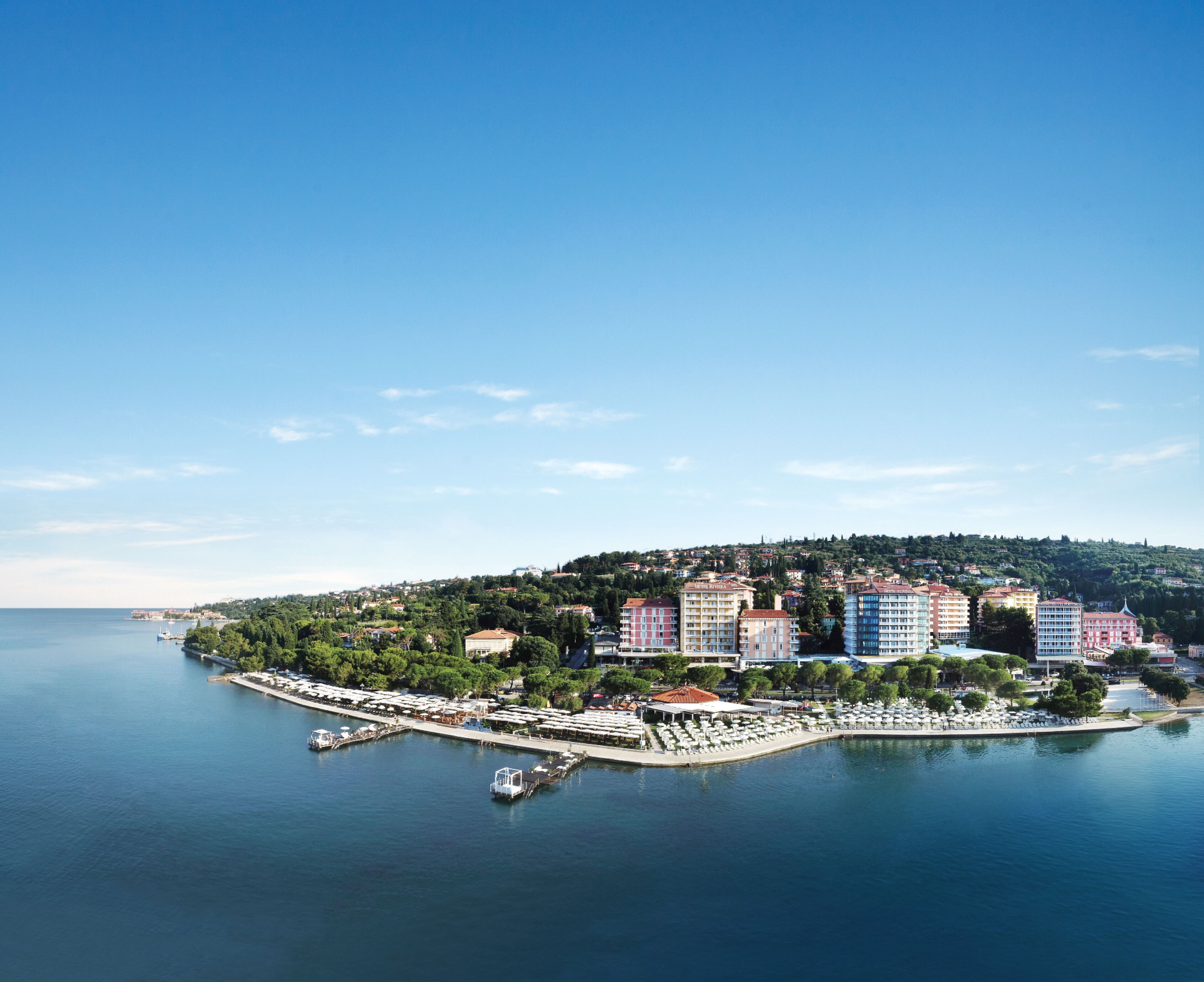 Un paisaje urbano costero con un puerto deportivo, edificios de varios pisos y un fondo montañoso.