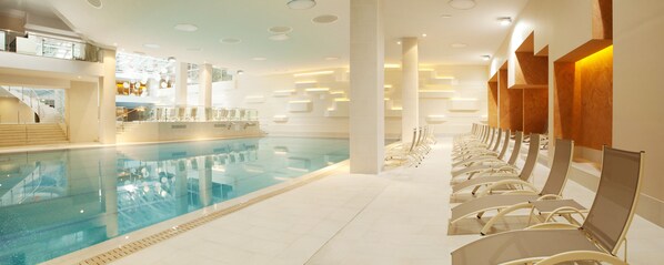 A modern indoor swimming pool with clear water, surrounded by lounge chairs and a staircase leading to upper levels.