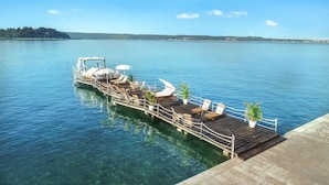 A wooden pier extending into a calm lake with clear water, offering a view of a distant forested hill.
