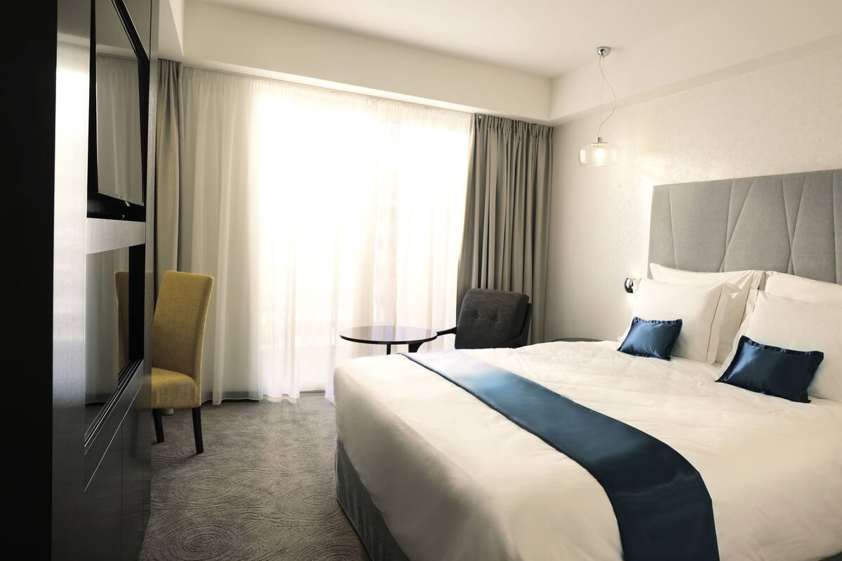 Habitación de hotel con una cama grande, una silla, una mesita y un espejo.